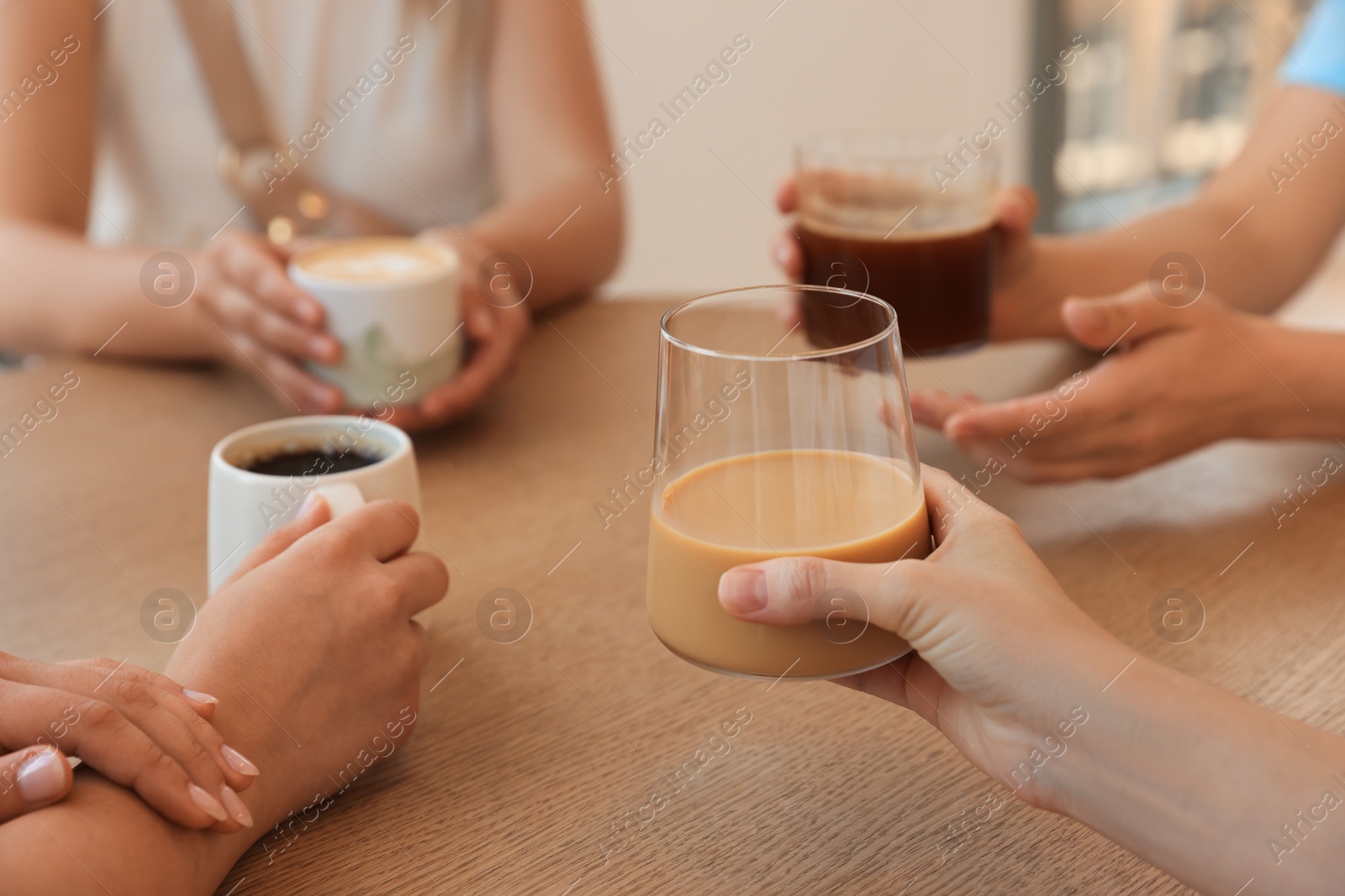 Photo of Friends drinking coffee at wooden table in cafe, closeup