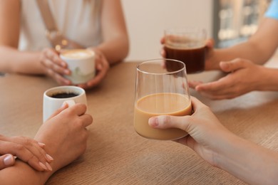 Friends drinking coffee at wooden table in cafe, closeup