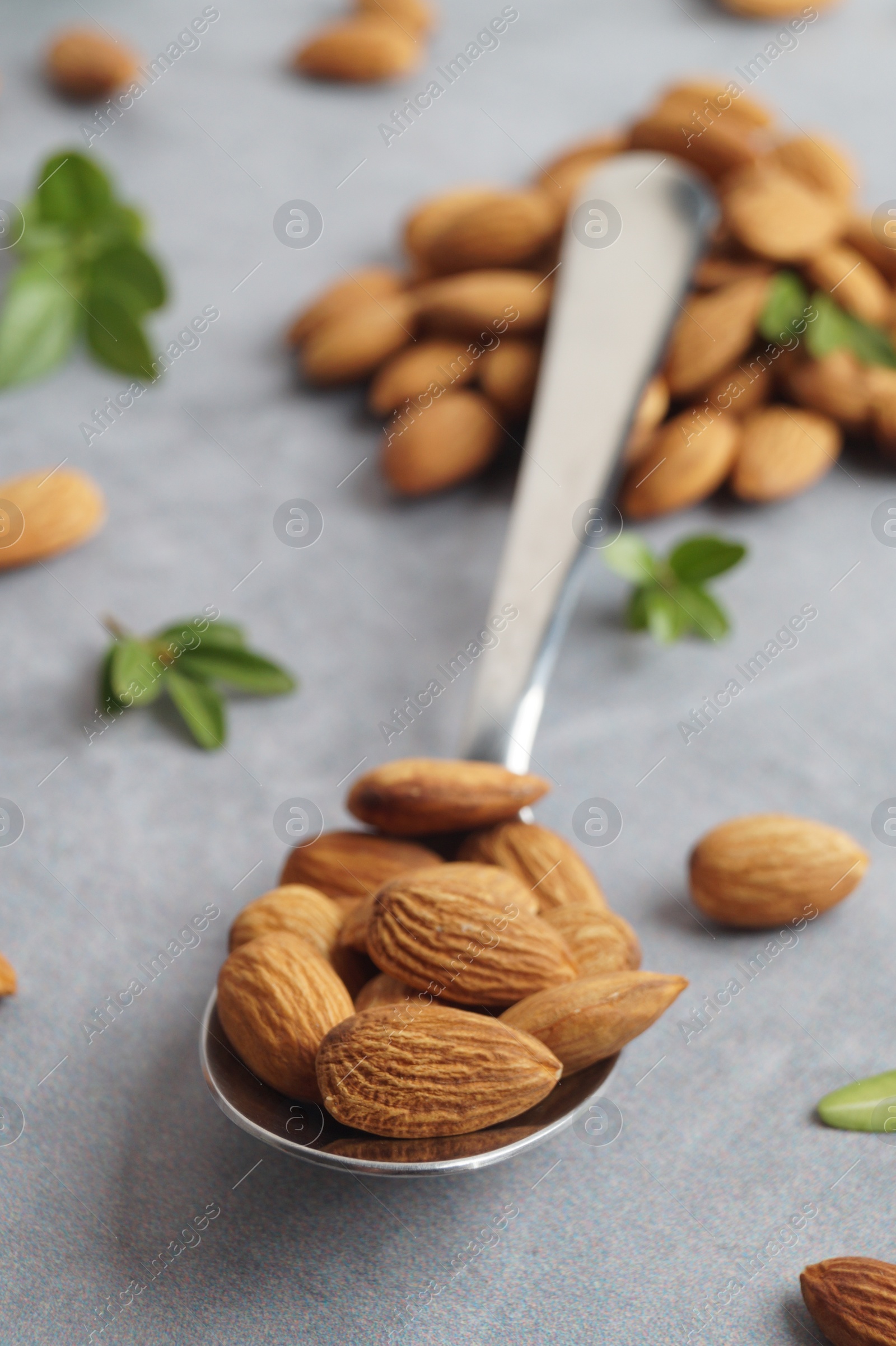 Photo of Spoon with tasty almonds and fresh green leaves on light grey table, closeup