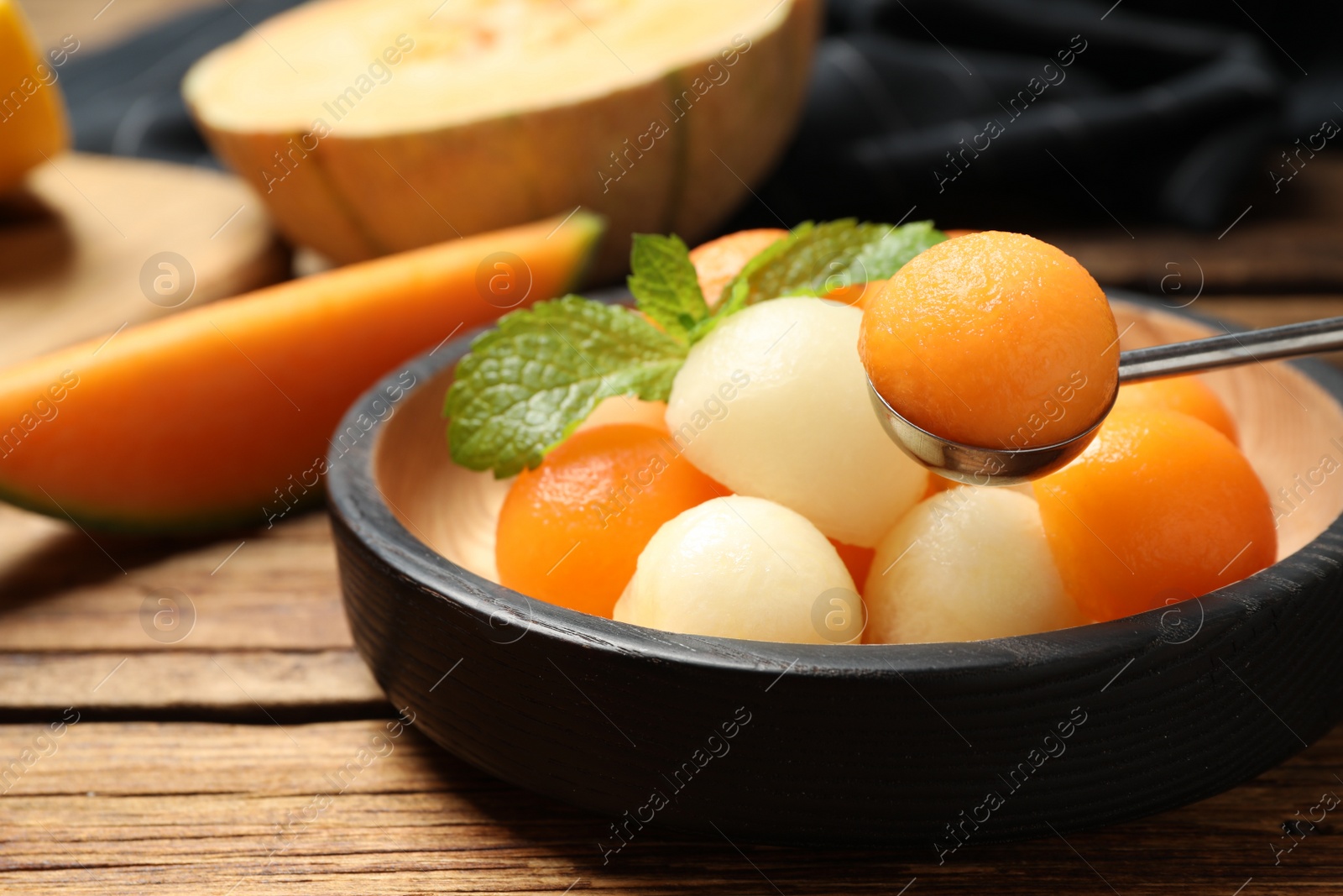 Photo of Different melon balls with mint on wooden table, closeup