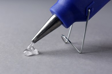 Photo of Melted glue dripping out of hot gun nozzle on grey background, closeup