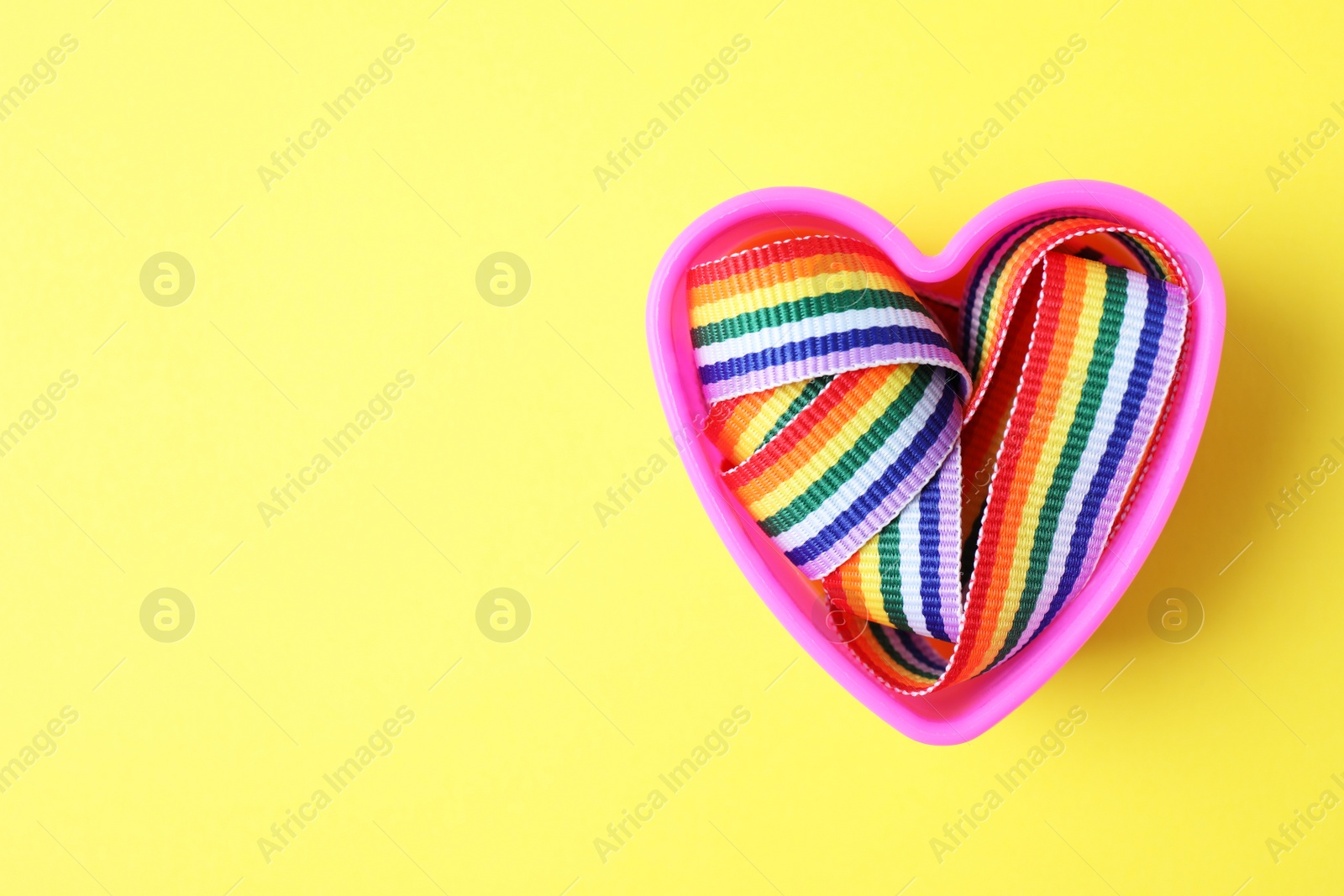 Photo of Heart shaped mold and bright rainbow ribbon on color background, top view with space for text. Symbol of gay community