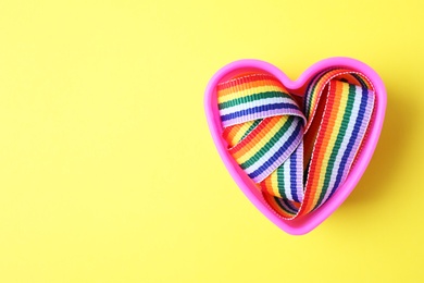 Photo of Heart shaped mold and bright rainbow ribbon on color background, top view with space for text. Symbol of gay community