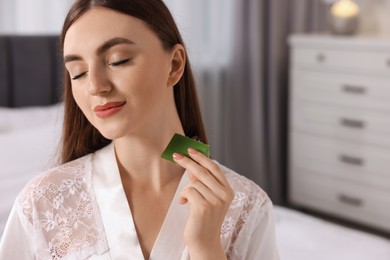 Photo of Young woman applying aloe gel from leaf onto her neck indoors. Space for text