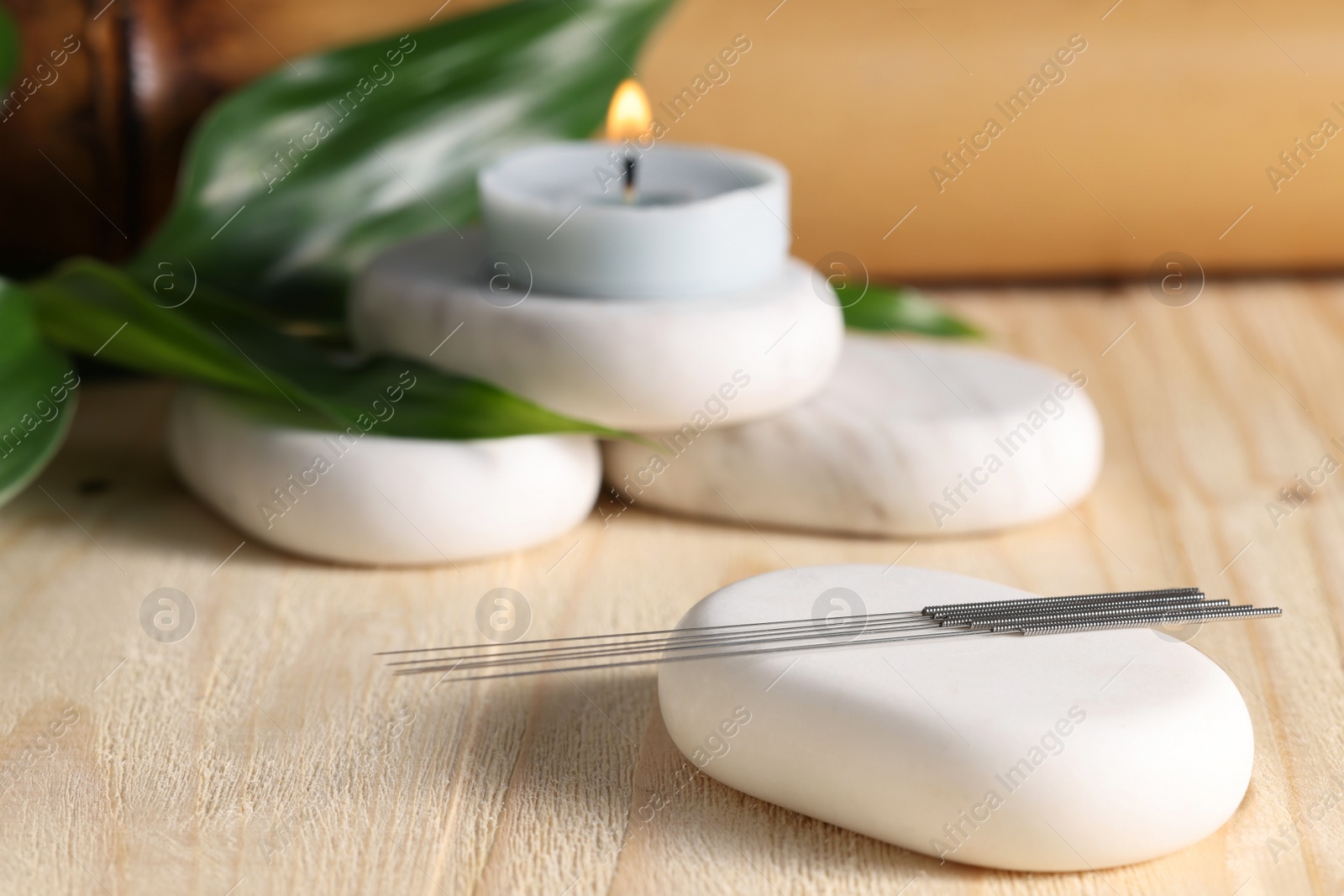 Photo of Stones with acupuncture needles and burning candle on wooden table, space for text