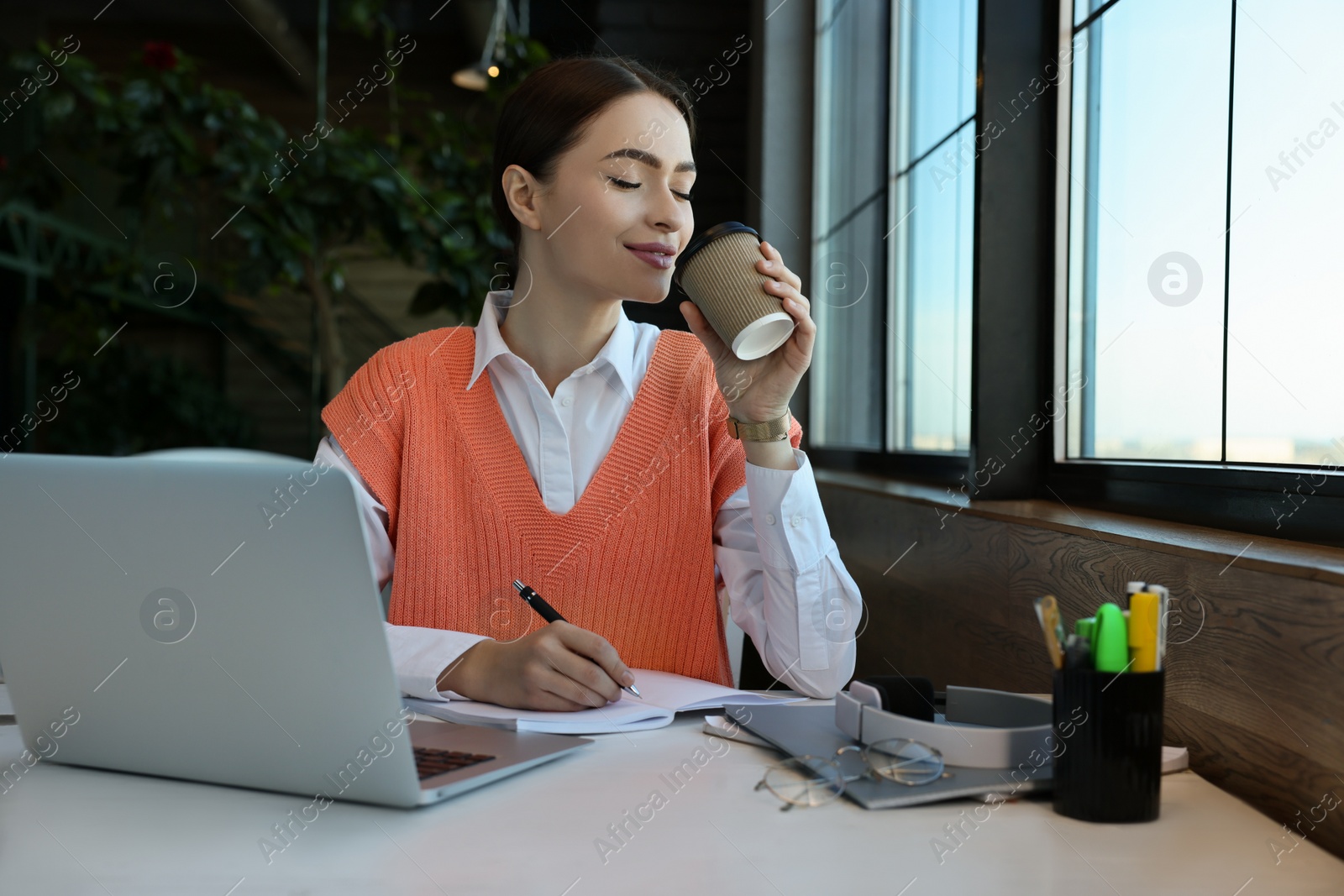 Photo of Young female student with laptop drinking coffee while studying at table in cafe