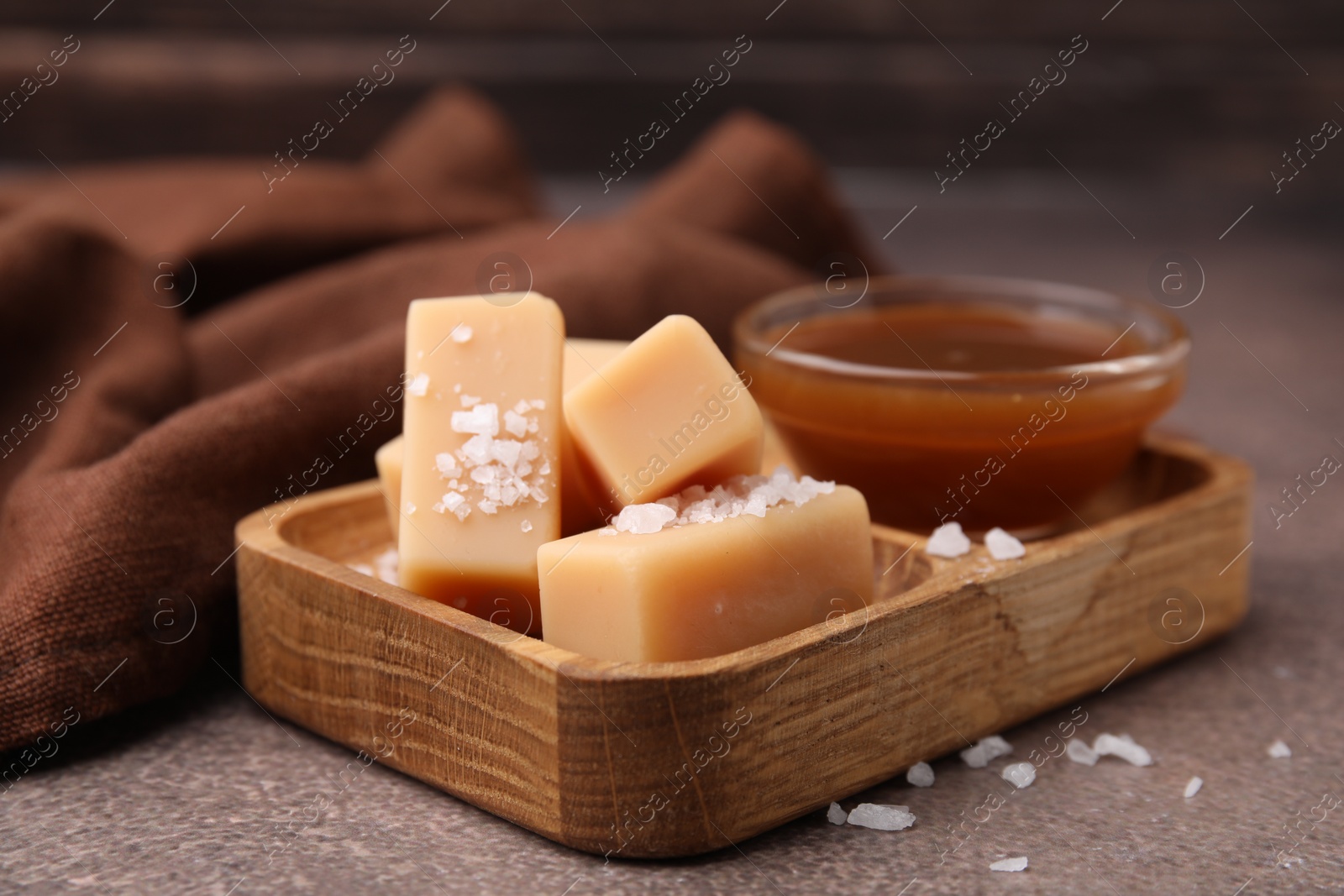 Photo of Yummy caramel candies, sauce and sea salt on brown table, closeup