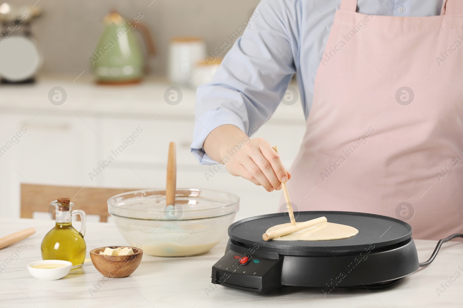 Photo of Woman cooking delicious crepe on electric pancake maker at white marble table in kitchen, closeup