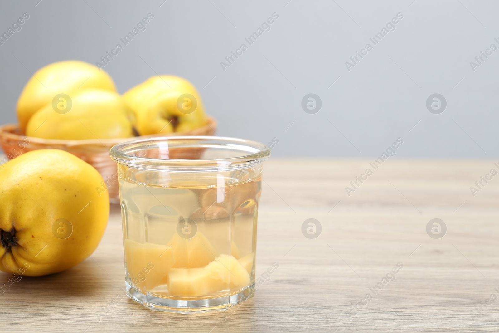 Photo of Delicious quince drink in glass and fresh fruits on wooden table, space for text