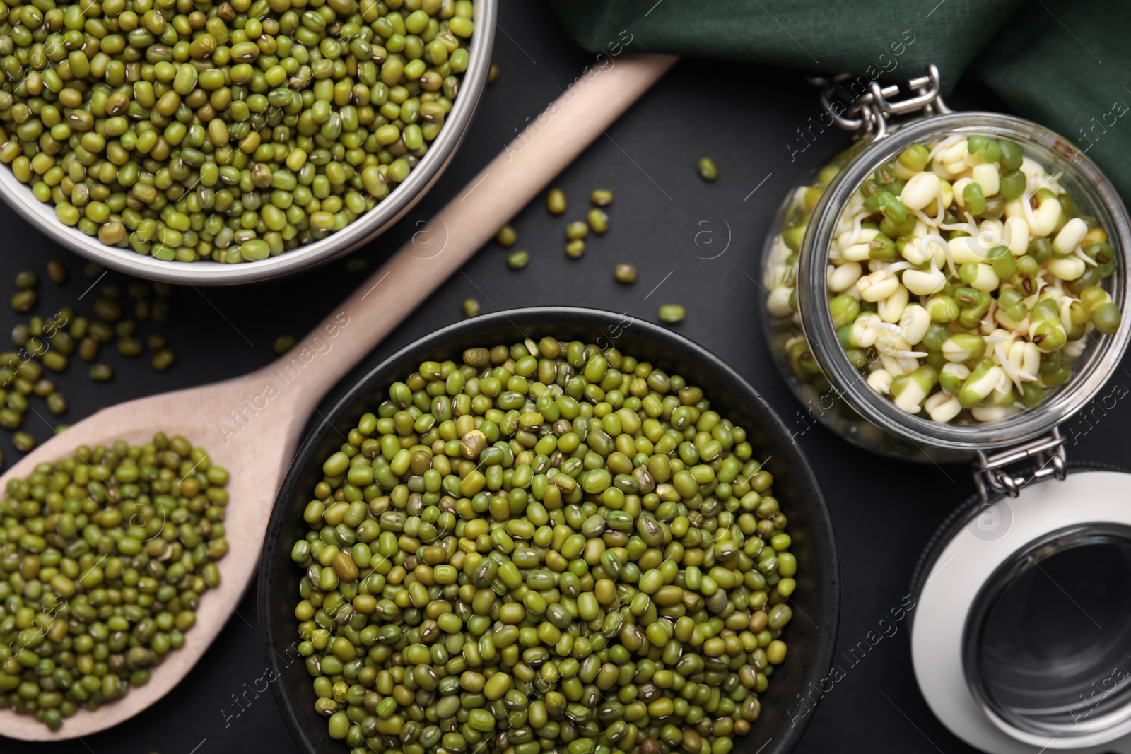 Photo of Different dishware with green mung beans on black background, flat lay