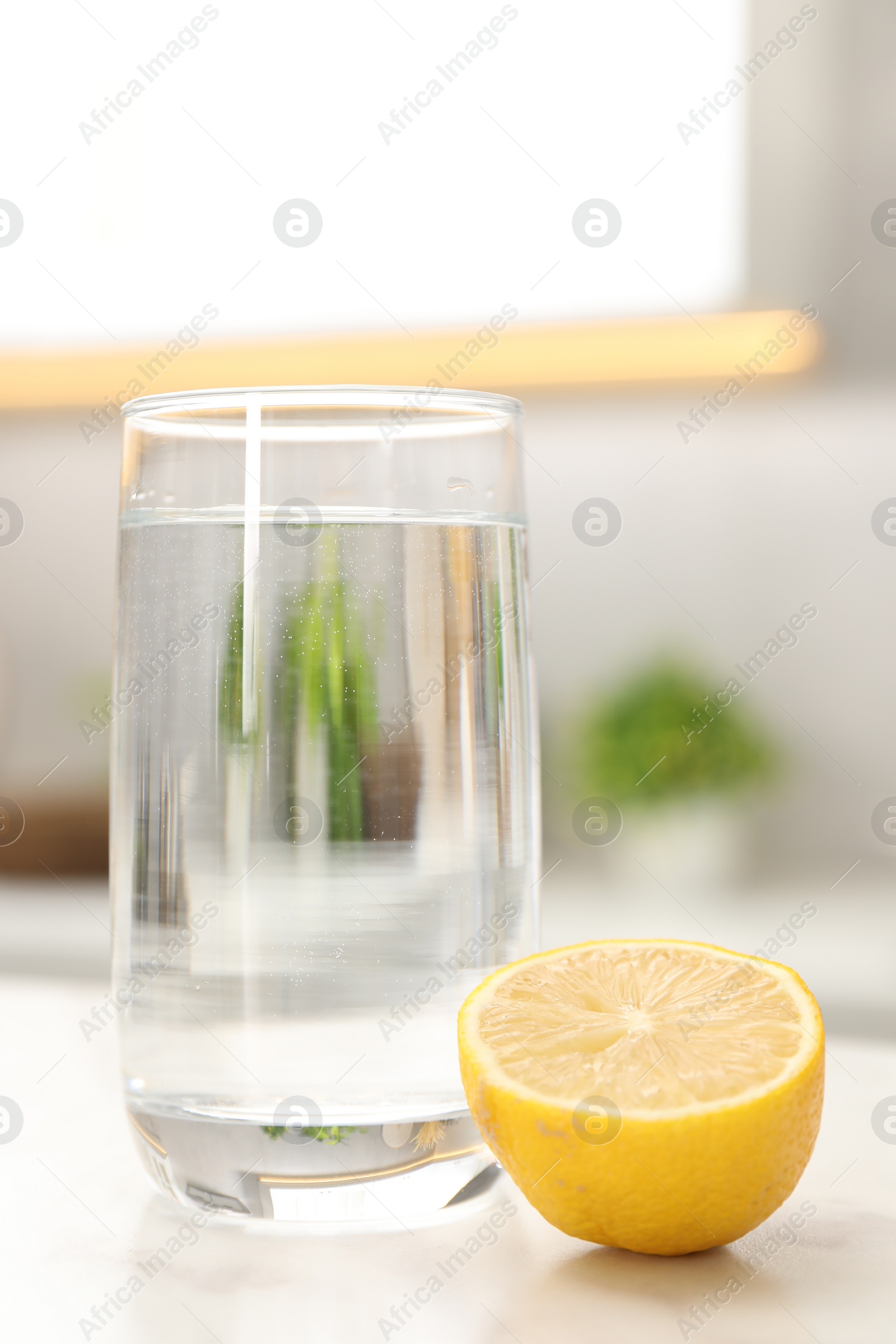 Photo of Glass with clear water and half of lemon on white table in kitchen