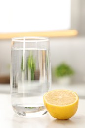 Photo of Glass with clear water and half of lemon on white table in kitchen