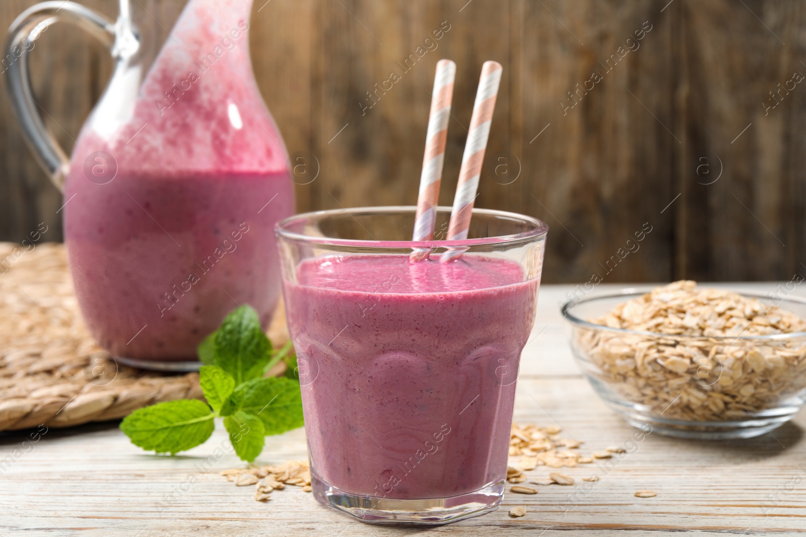 Photo of Glass of blackberry smoothie with straws, mint and oatmeal on light wooden table