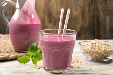 Photo of Glass of blackberry smoothie with straws, mint and oatmeal on light wooden table