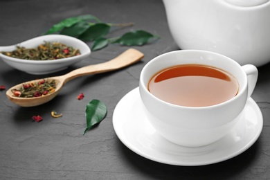 Photo of Cup of tea with dried and fresh leaves on black table. Space for text