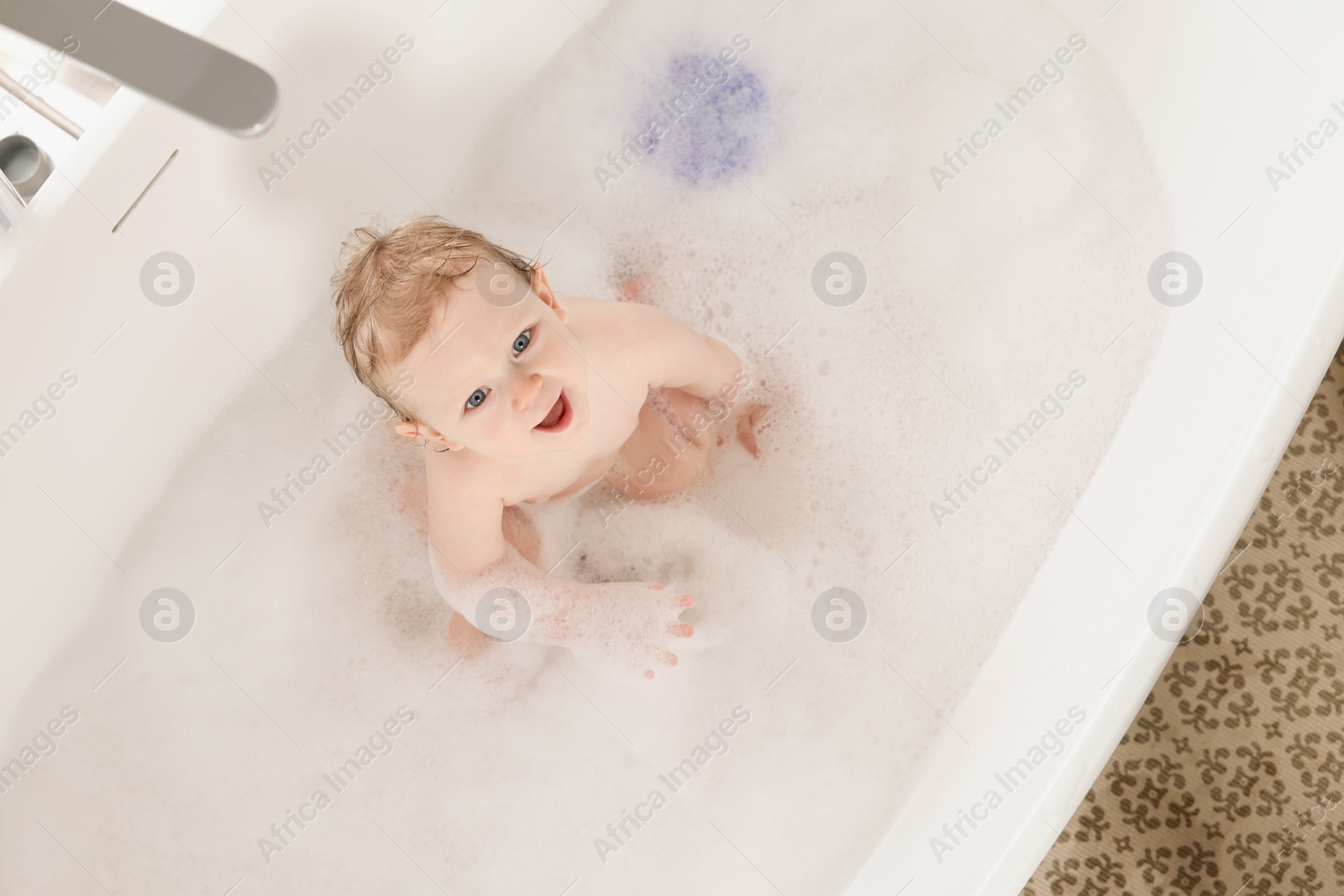Photo of Cute little baby bathing in tub at home, top view
