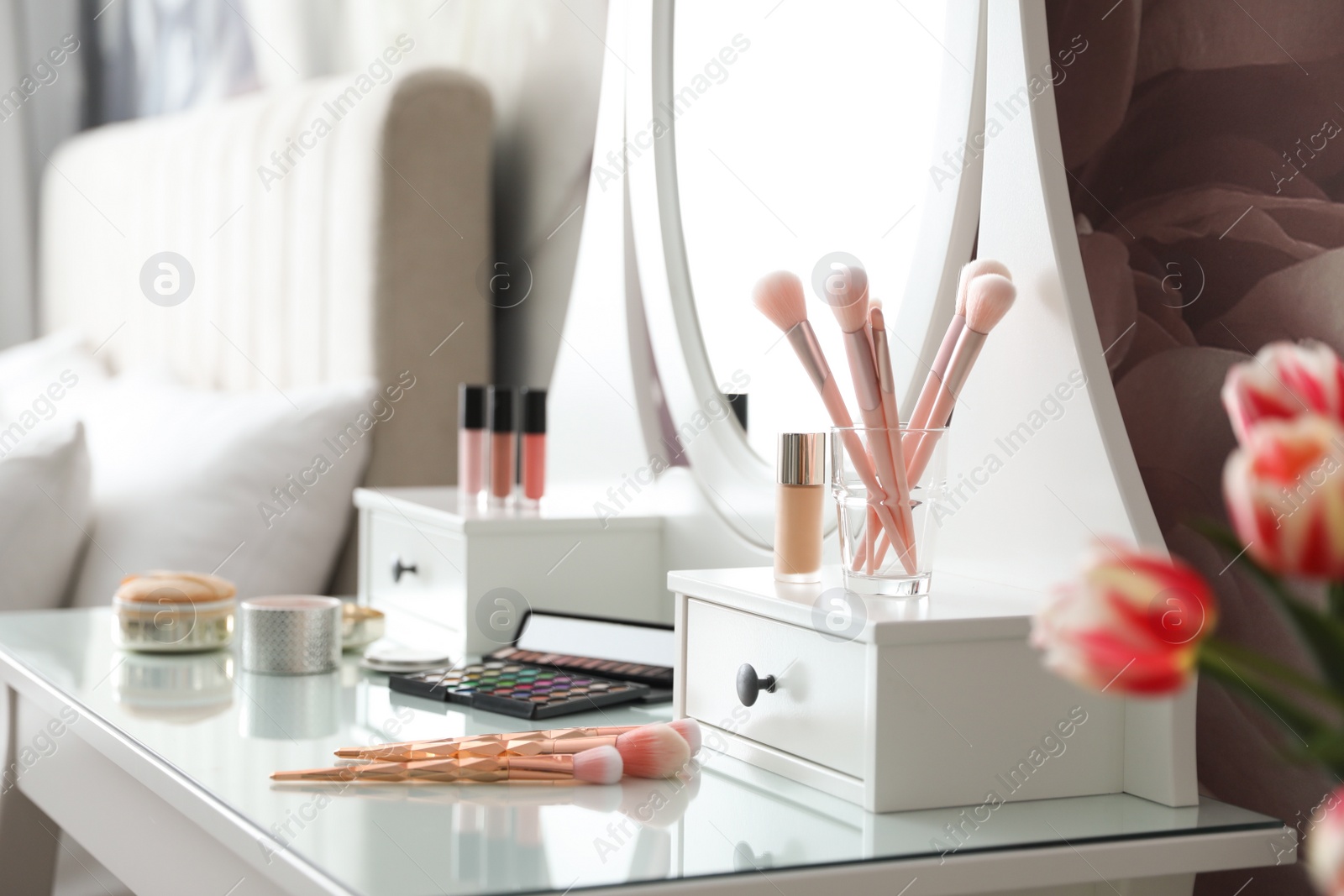 Photo of Set of makeup products and cosmetic brushes on dressing table indoors. Interior design