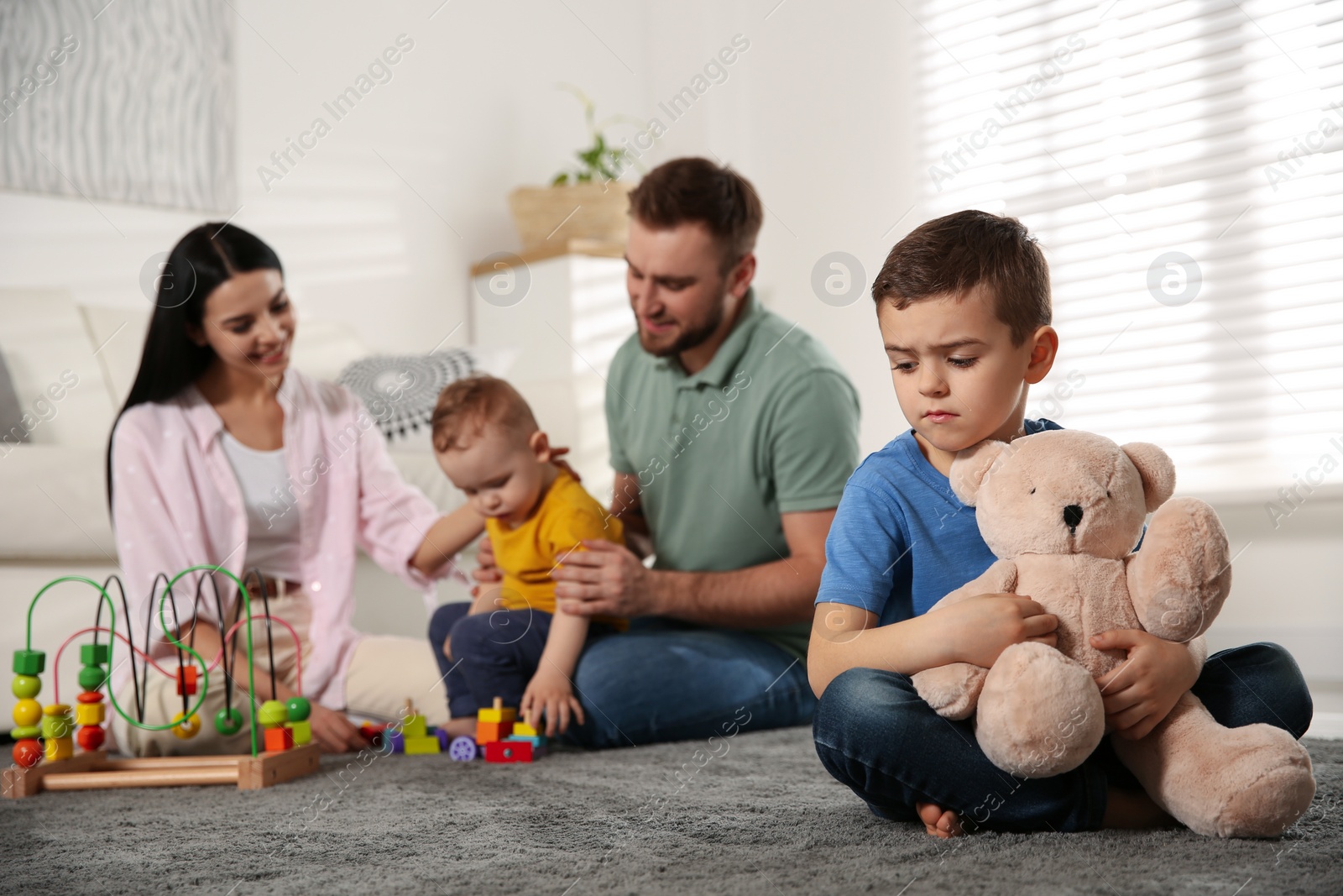 Photo of Unhappy little boy feeling jealous while parents spending time with his baby brother at home