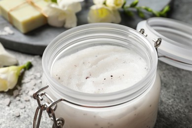Body scrub in glass jar on grey table, closeup