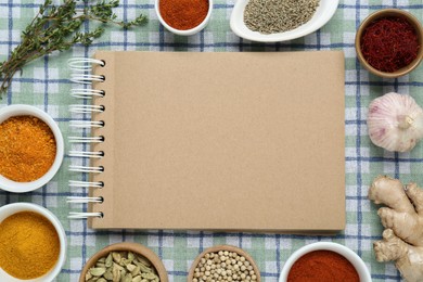 Photo of Blank recipe book surrounded by different ingredients on checkered tablecloth, flat lay. Space for text