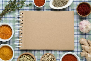 Blank recipe book surrounded by different ingredients on checkered tablecloth, flat lay. Space for text