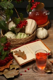 Photo of Delicious viburnum tea, books and pumpkins on wooden table. Cozy autumn atmosphere
