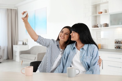 Young woman and her mature mother taking selfie at table indoors