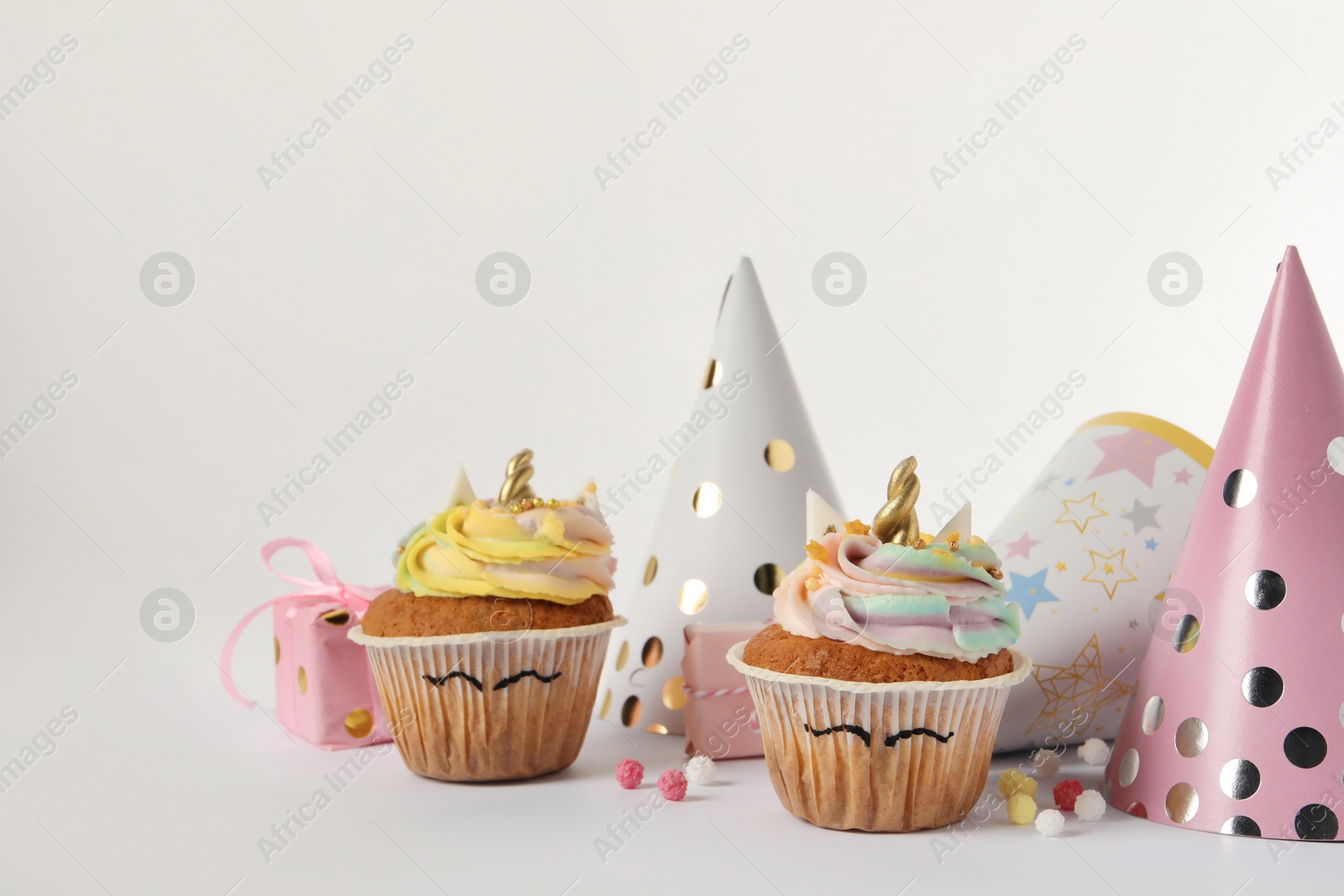 Photo of Cute sweet unicorn cupcakes and party hats on white background, space for text