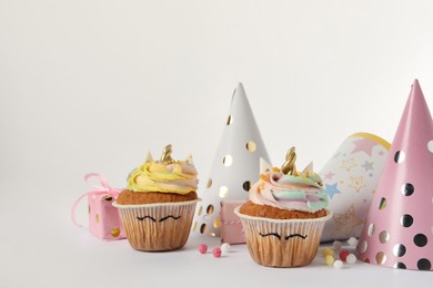 Photo of Cute sweet unicorn cupcakes and party hats on white background, space for text
