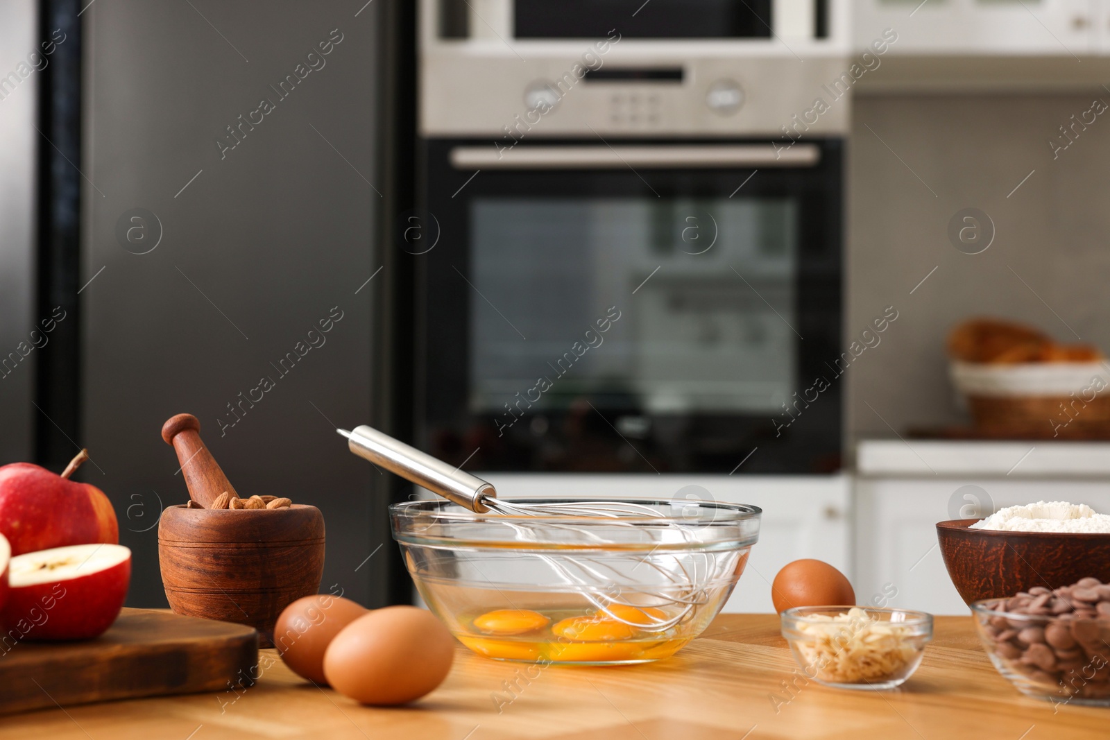 Photo of Cooking process. Metal whisk, bowl and products on wooden table in kitchen