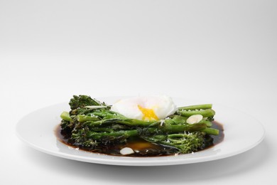 Photo of Tasty cooked broccolini with poached egg, almonds and sauce on white background, closeup