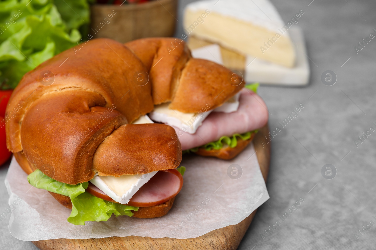 Photo of Tasty crescent roll with brie, ham and lettuce on grey table, closeup. Space for text