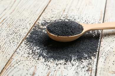 Poppy seeds in spoon on white wooden table