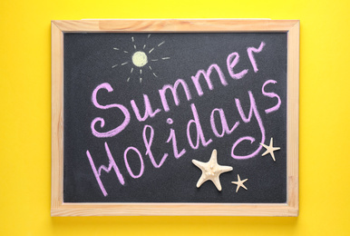 Chalkboard with phrase SUMMER HOLIDAYS on yellow background, top view. School's out