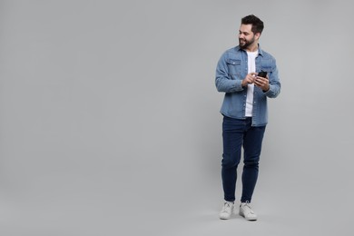 Photo of Happy young man using smartphone on grey background, space for text