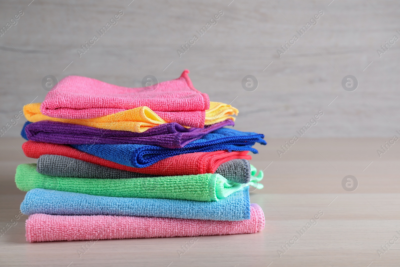 Photo of Stack of colorful microfiber cloths on light wooden table, space for text