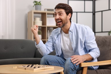 Emotional man playing checkers in armchair at home
