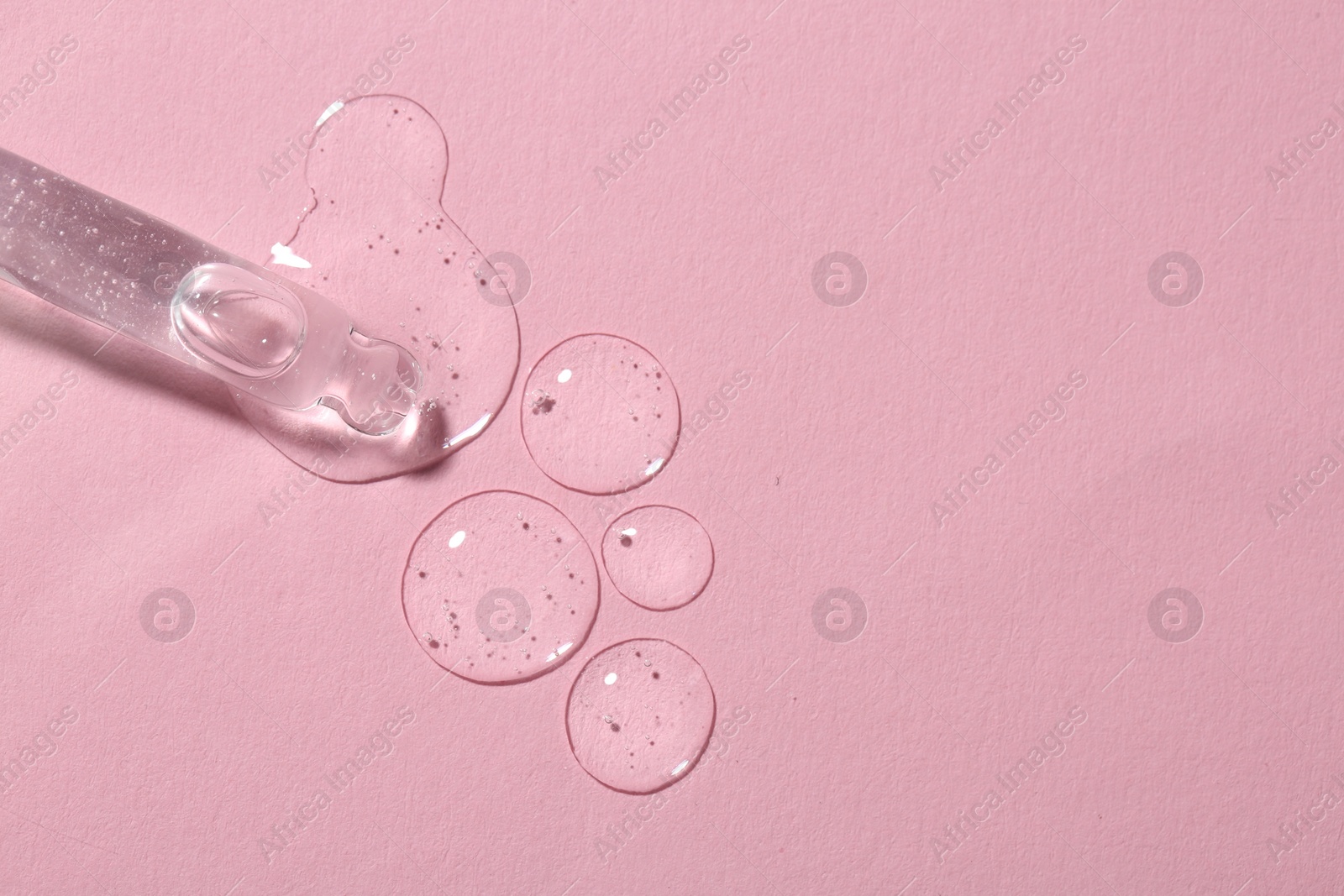 Photo of Dripping cosmetic serum from pipette onto pink background, top view. Space for text