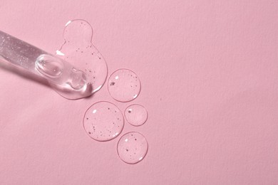 Dripping cosmetic serum from pipette onto pink background, top view. Space for text