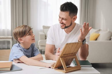 Photo of Boy with father doing homework using tablet at table in living room
