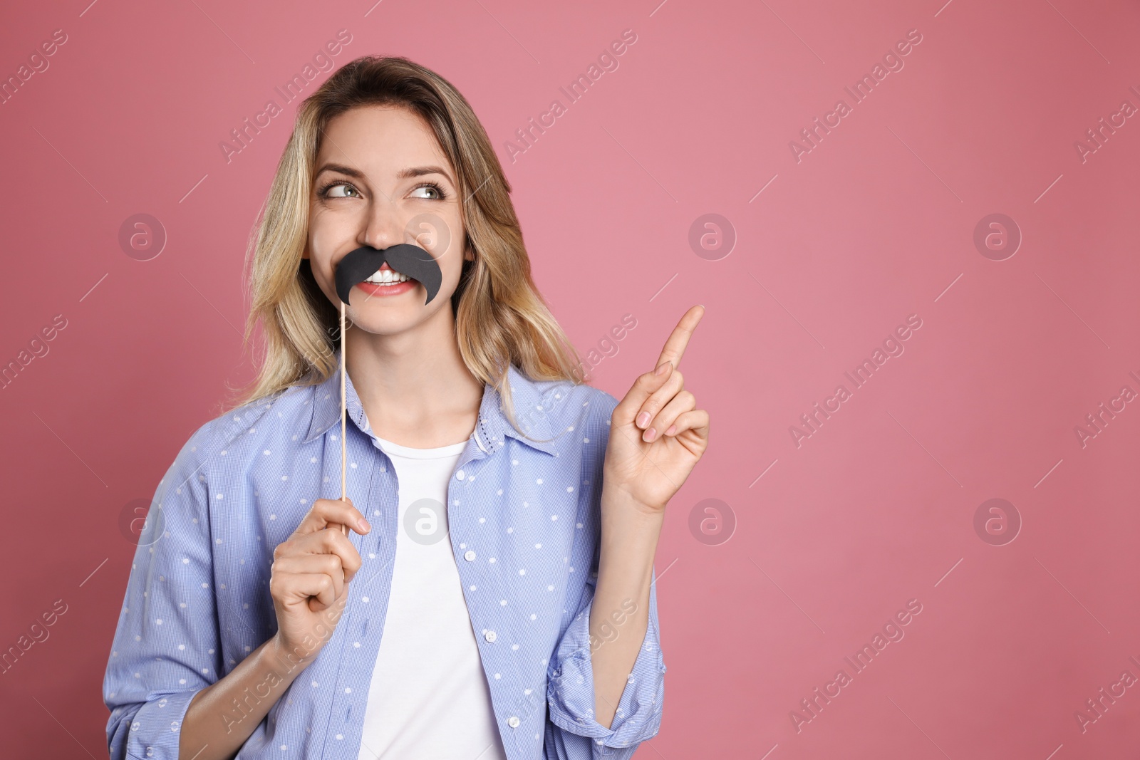 Photo of Funny woman with fake mustache on dusty rose background, space for text