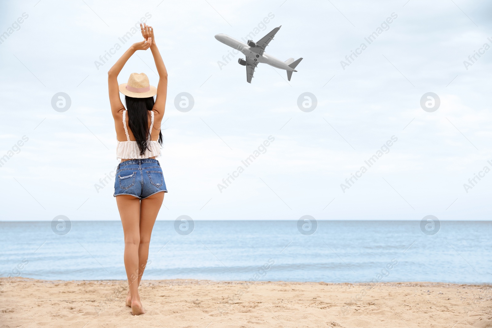 Image of Woman on beach looking at airplane flying in sky, back view