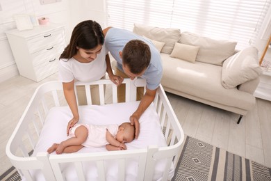 Happy couple near crib with their cute baby at home