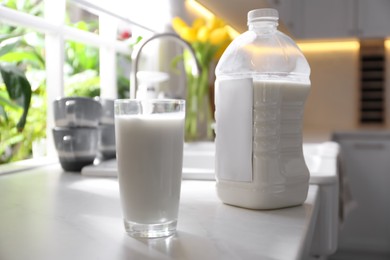 Photo of Gallon bottle of milk and glass on white countertop in kitchen