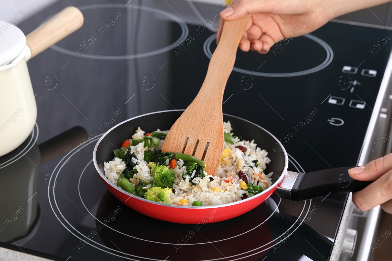Photo of Woman frying rice with vegetables at induction stove, closeup