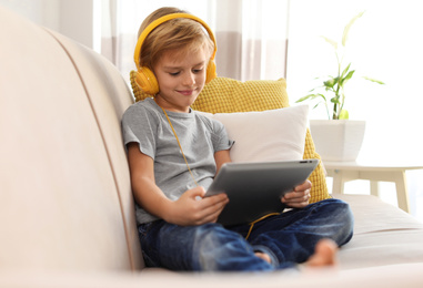 Cute little boy with headphones and tablet listening to audiobook at home