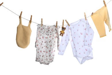 Different baby clothes and bear toy drying on laundry line against white background