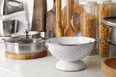 Photo of Metal colander, other cooking utensils and raw pasta on countertop in kitchen