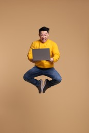 Photo of Happy man with laptop jumping on beige background