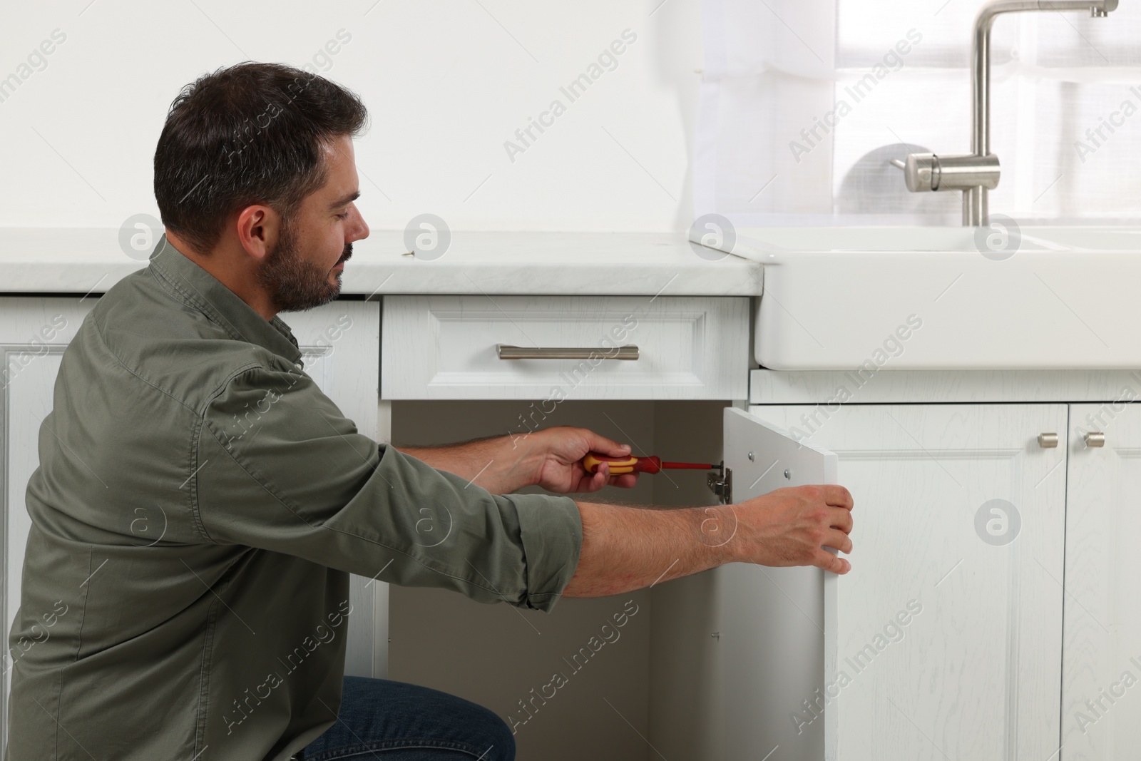 Photo of Man with screwdriver assembling furniture in kitchen